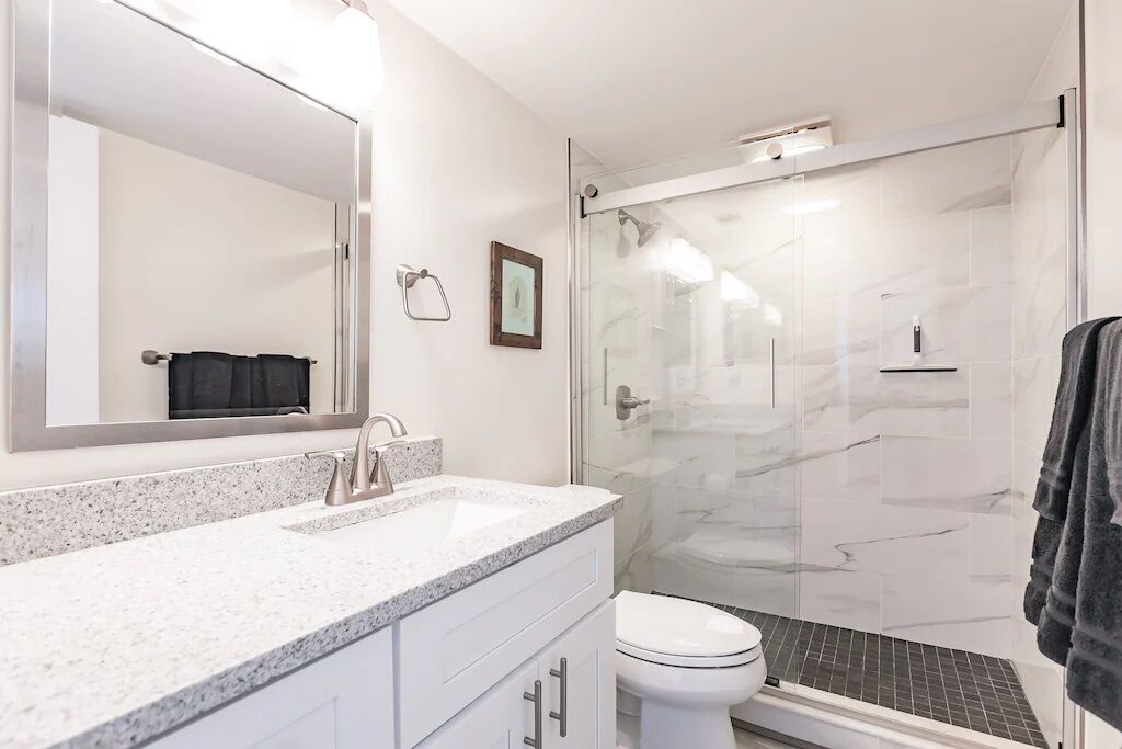 A modern bathroom with a glass-enclosed shower, a white sink, and a large mirror.