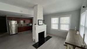 A spacious kitchen with a white brick fireplace, wooden cabinets, and a stainless steel refrigerator. - Walk to the Beach! Two bedroom cottage in Swifts Beach community. (Wareham)