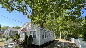 A single-story mobile home with a white exterior, a chimney, and a small front yard with a stop sign, a mailbox, and a few potted plants. - Walk to the Beach! Two bedroom cottage in Swifts Beach community. (Wareham)
