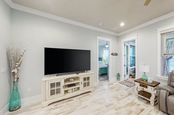 A living room with a flat-screen TV on a white cabinet, a vase with dried branches, and a wooden coffee table.