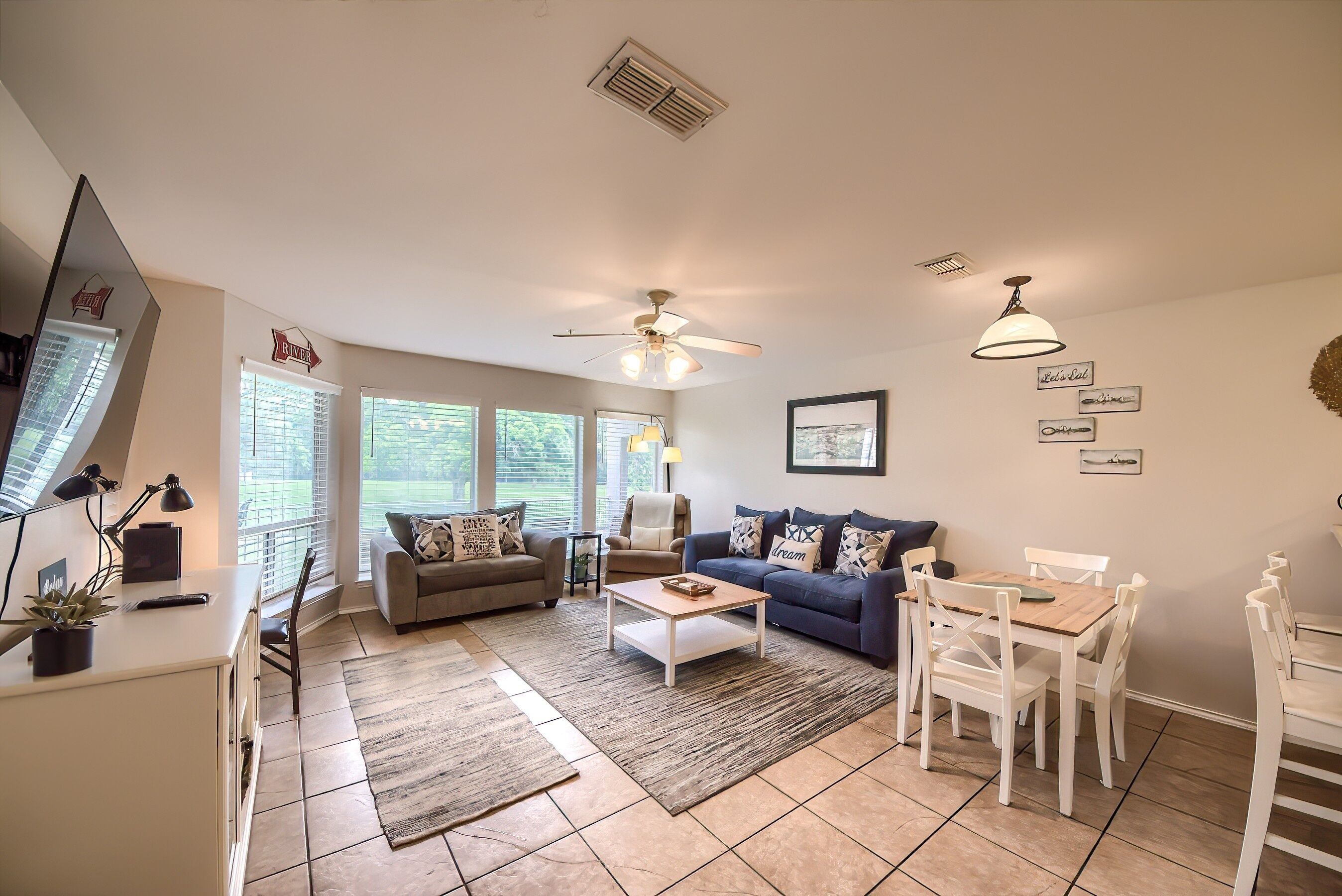 A spacious living area with a ceiling fan, a dining table with chairs, a sofa, and a coffee table.