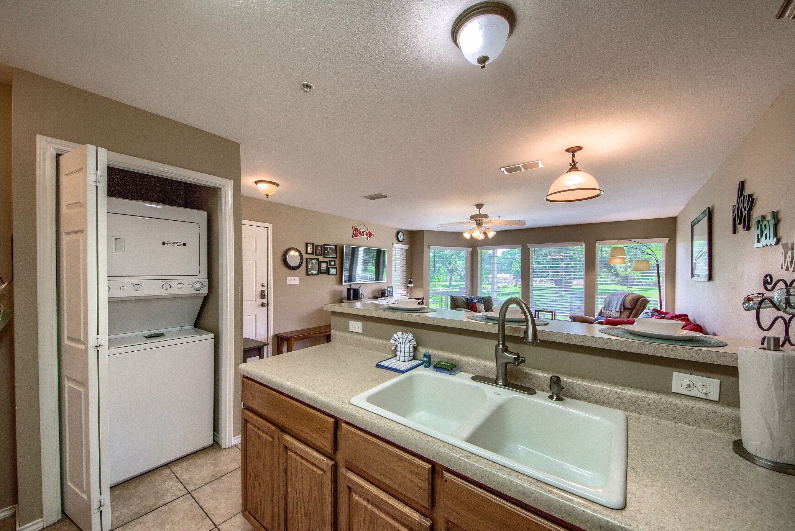 A kitchen with a built-in washer and dryer, a sink, and a window overlooking a garden.
