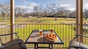 Ein Tisch mit zwei Biergläsern und einem Brezel auf einem Balkon mit Blick auf einen Park.