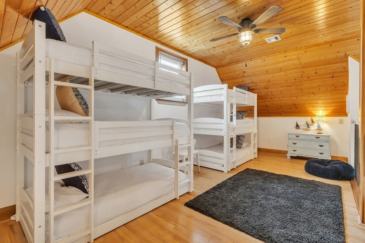 A room with bunk beds, a ceiling fan, a small table with a lamp, and a dark rug.