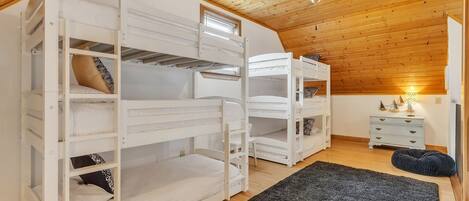 A room with bunk beds, a ceiling fan, a small table with a lamp, and a dark rug.