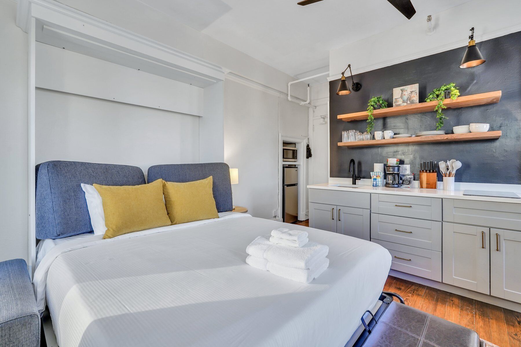 A modern bedroom with a large bed, a kitchenette, and a dark accent wall.