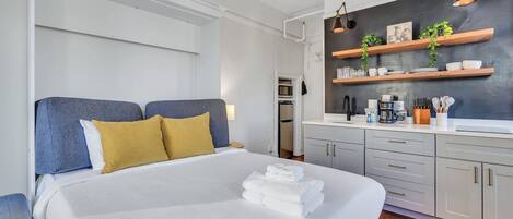 A modern bedroom with a large bed, a kitchenette, and a dark accent wall.