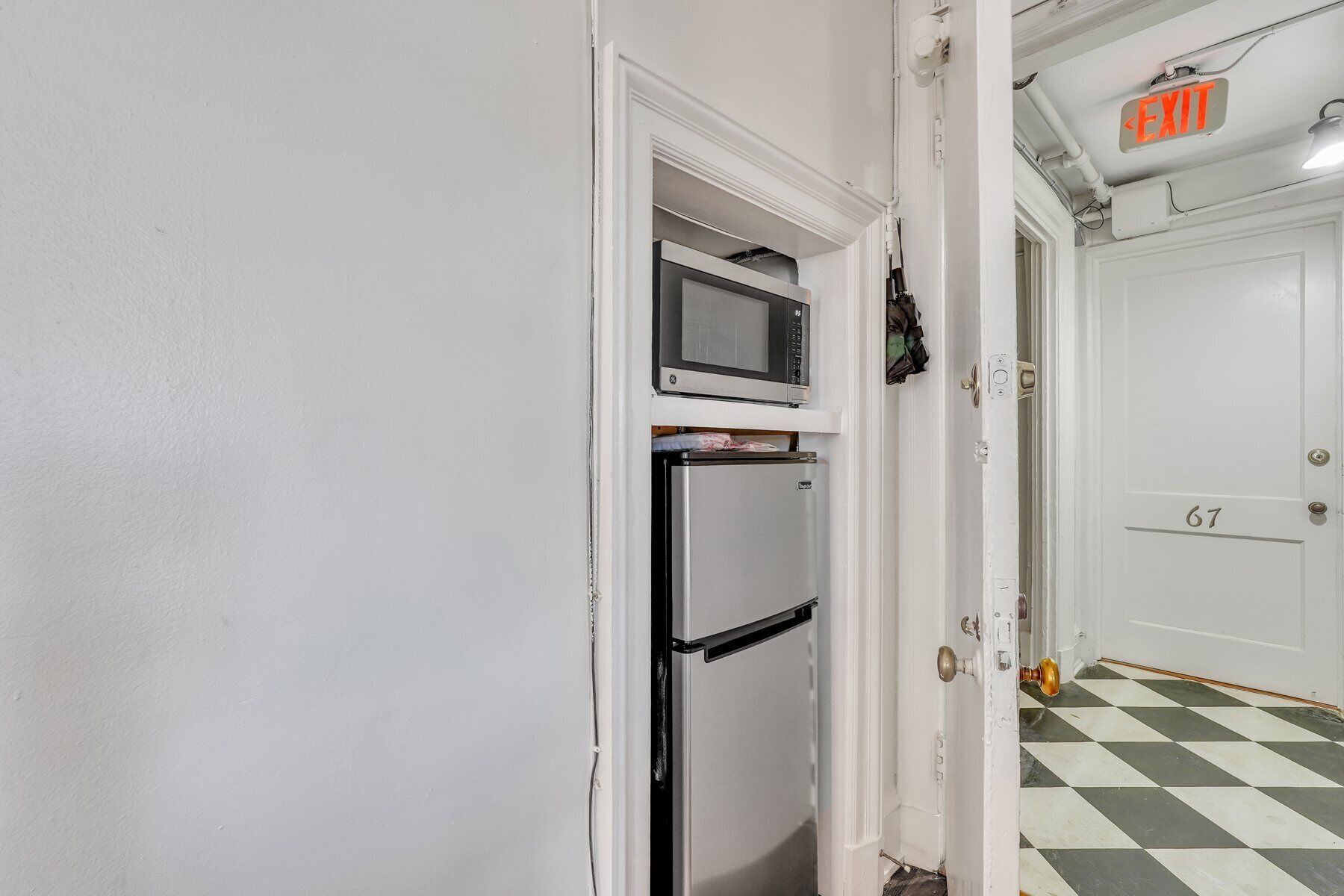 Un couloir avec une porte blanche portant le numéro « 67 » et un panneau indiquant la sortie au-dessus.