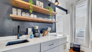 Una cocina moderna con armarios blancos, encimera negra y estantes de madera con plantas.