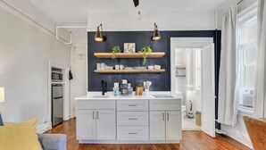 Una cocina moderna con armarios blancos, estantes de madera e iluminación colgante.