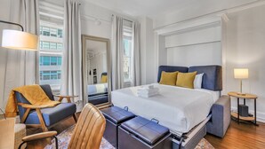 Habitación de hotel con una cama grande, un escritorio, una silla, una mesita y una ventana con cortinas.