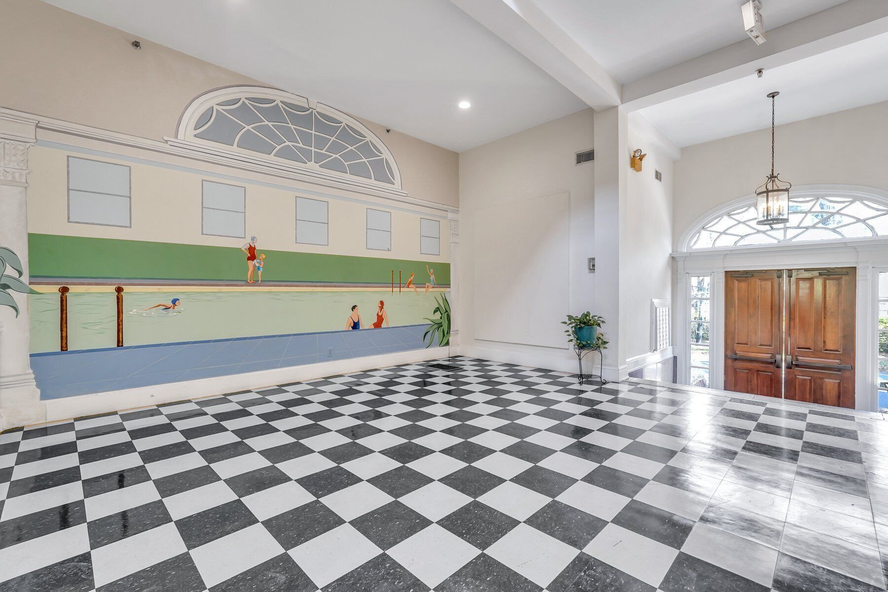 A spacious lobby with a checkered floor, a pool area with a mural, and a large arched window.