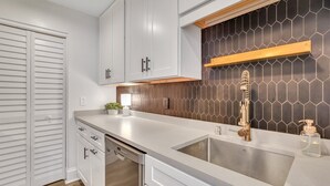 A modern kitchen with white cabinetry, a stainless steel sink, and a hexagonal tile backsplash. - Unbeatable Location in Heart of Historic Savannah by Lucky Savannah (Savannah)