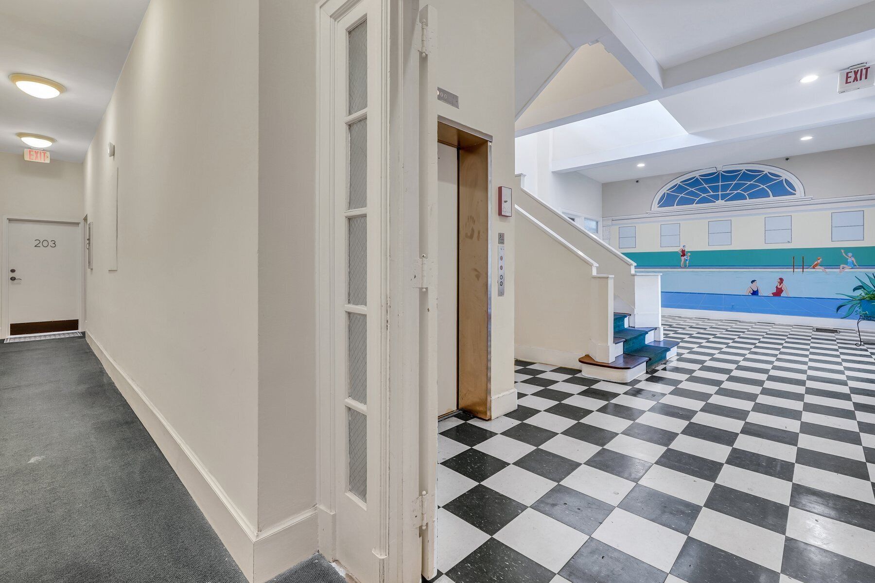 Un hall d’hôtel avec un sol à carreaux, un escalier menant à un espace piscine et un ascenseur.