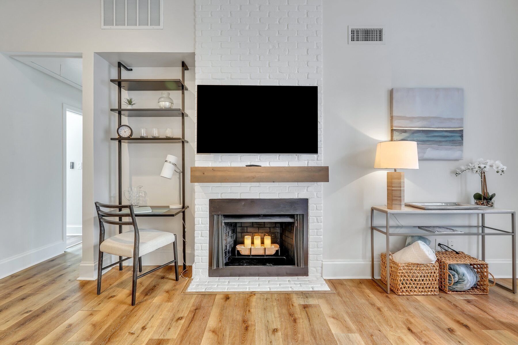 A modern living room with a fireplace, a TV mounted above it, a desk with a chair, and wicker baskets.