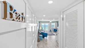 Un couloir avec une pancarte indiquant « Plage », un canapé bleu et une vue sur l’océan par de grandes fenêtres.