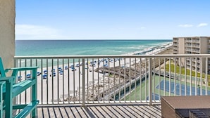 Un balcon avec vue sur une plage, un court de tennis et un immeuble.