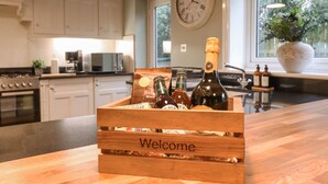 Una caja de madera con la palabra "Welcome" sobre una encimera de cocina, que contiene botellas y un saco de pan.