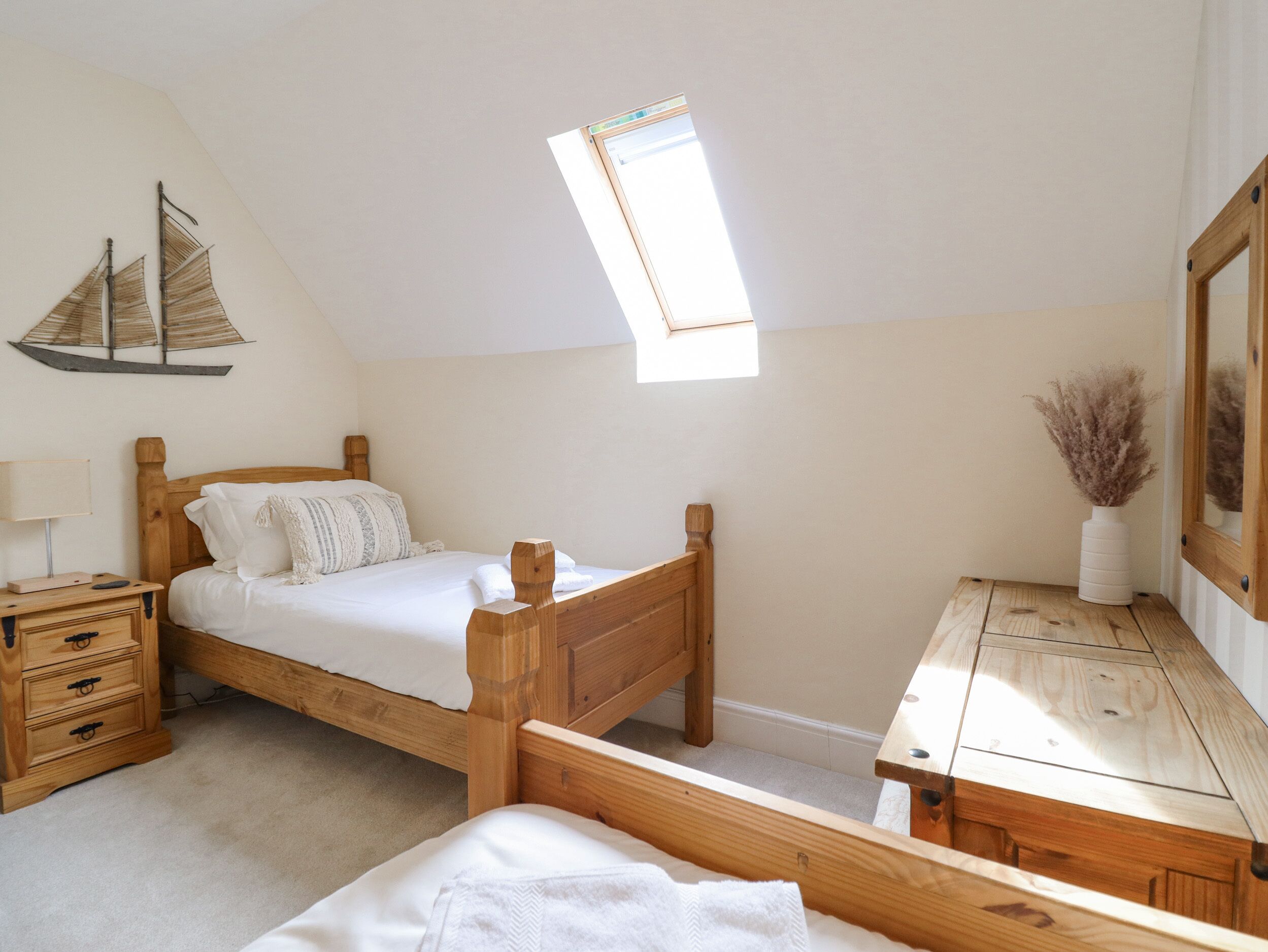 Un dormitorio con cama de madera, una mesita de noche, un aparador, una pequeña mesa y una ventana con vista al cielo.