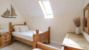Un dormitorio con cama de madera, una mesita de noche, un aparador, una pequeña mesa y una ventana con vista al cielo.