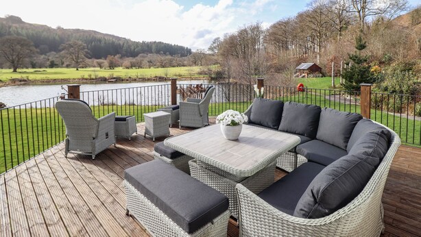 Una terraza con muebles de mimbre, una mesa y vistas a un lago y colinas.