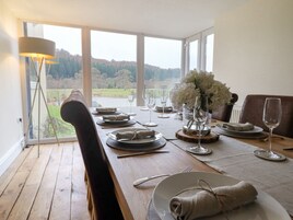 A dining table set for four with a view of a lake and forest through large windows.