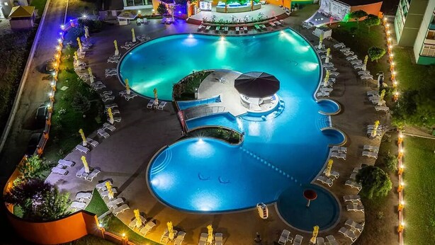 A large, well-lit swimming pool with multiple lounge areas and a central water feature. - Hotel Balada (Saturn)