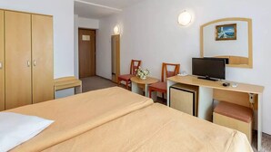 A hotel room with a bed, a desk with a television, a chair, and a small table with a vase. - Hotel Balada (Saturn)