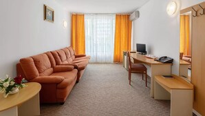 A hotel room with a sofa, a desk, a chair, a TV, and a mirror. - Hotel Balada (Saturn)