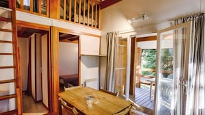 A wooden dining table with chairs, a loft bedroom with a wooden railing, and a sliding glass door leading to an outdoor deck. - 6-person chalet (Laruns)