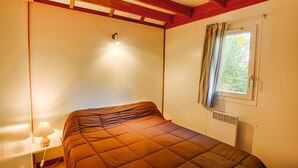 A bedroom with a bed, a nightstand with a lamp, a window with curtains, and a ceiling light. - 6-person chalet (Laruns)