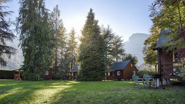 A cabin with a wooden deck, surrounded by tall trees and a mountain in the background. - 6-person chalet (Laruns)