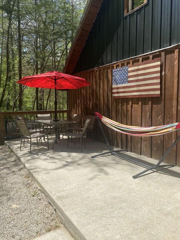 An outdoor patio with a table and chairs, a red umbrella, and a hammock.