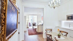 Eine moderne Küche mit weißen Schränken, einer Mikrowelle und einem Spülbecken. Ein Essbereich mit einem Holztisch und Stühlen lädt ein, und eine Kronleuchter hängt darüber.