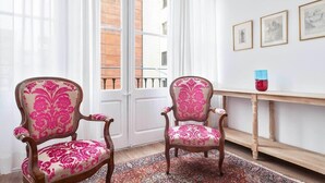 Ein Zimmer mit zwei stilsicheren Sesseln mit rosa Polsterung, einem Holztisch mit roter Vase und einem gemusterten Teppich.