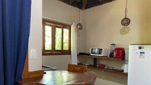 Cuina compacta amb taula i cadires de fusta, microones, cafetera vermella i nevera blanca.