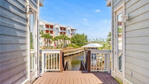 A wooden deck leading to a canal with a bridge, surrounded by buildings with balconies and a clear sky.