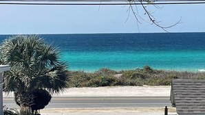 Vista costera con playa, camino, cerca blanca y un edificio de pared de ladrillo.