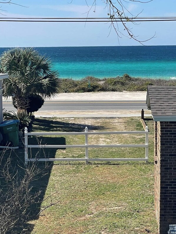 Une vue sur la côte, avec une plage, une route, une clôture blanche et un bâtiment doté d’un mur en briques.
