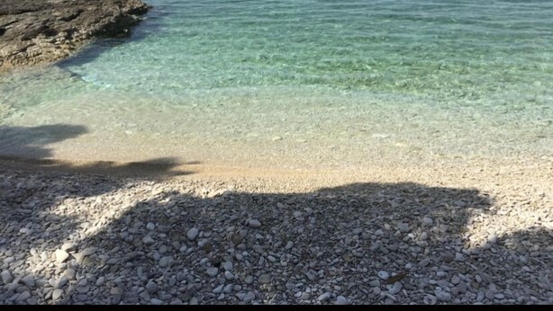 Een kiezelstrand met helder water en een rotsachtige landtong.