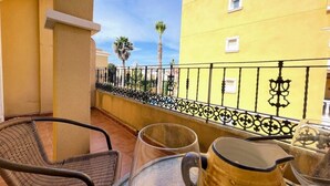 A balcony with wicker chairs, a table with a pitcher and a glass, and a yellow building with a black railing in the background. - Pleasant 4 Bedroom Townhouse with Com Pool VM7 (Orihuela)