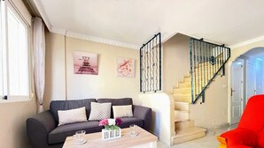 A living room with a sofa, coffee table, and a red chair. There is a staircase with a black railing. - Pleasant 4 Bedroom Townhouse with Com Pool VM7 (Orihuela)