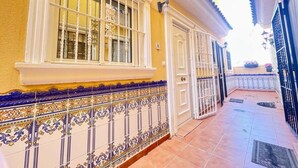 A yellow building with a tiled balcony, a white door, and a window with metal bars. - Pleasant 4 Bedroom Townhouse with Com Pool VM7 (Orihuela)