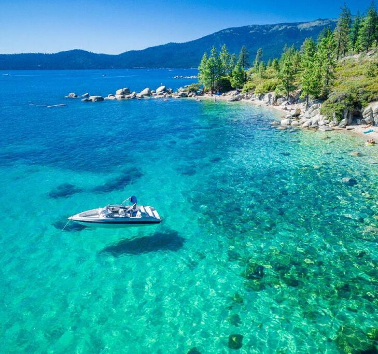 Um lago azul límpido com um barco e margem rochosa.