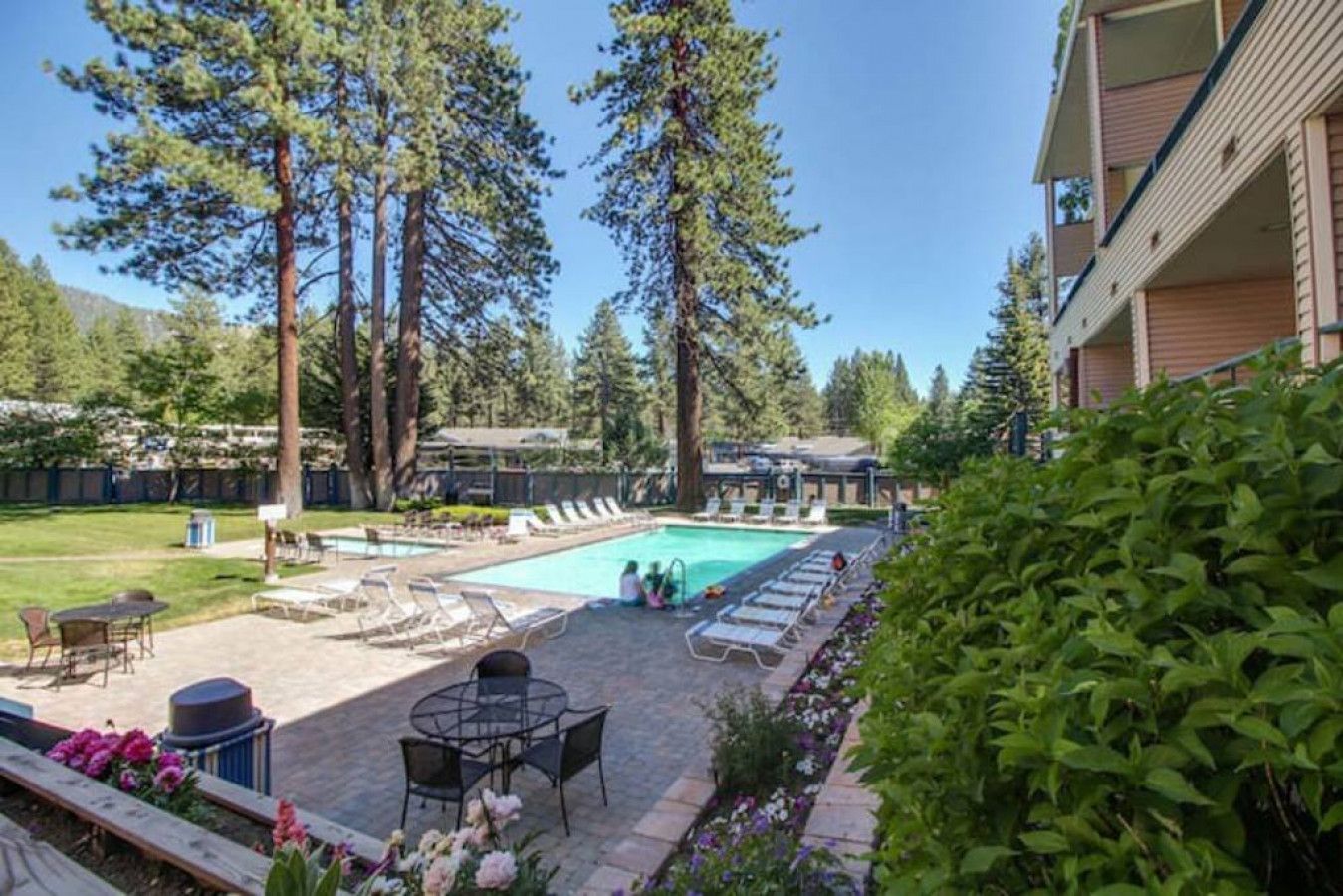 A pool area with lounge chairs, a table, and a small garden with flowers.