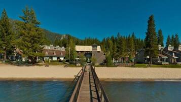 A wooden boardwalk leading to a building with a large overhang, surrounded by trees and a clear sky.
