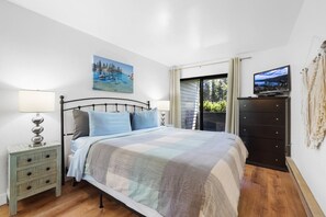 Un dormitorio con cama, mesita de noche, cómoda, televisor y un cuadro en la pared.