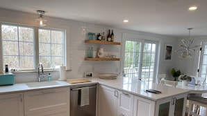 Una cocina moderna con armarios blancos, encimera de madera y lavavajillas integrado. Hay ventanas que ofrecen luz natural y vistas al exterior.