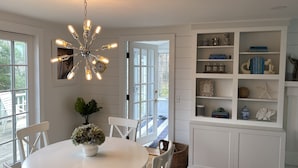 Un comedor con una mesa redonda, sillas, una planta en maceta, una lámpara de pared y una estantería empotrada con objetos decorativos.