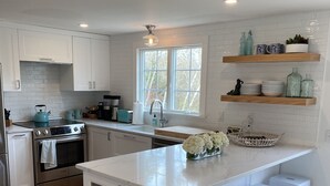 Cocina moderna con armarios blancos, una isla central con taburetes, un ventanal y estantes empotrados con objetos decorativos.